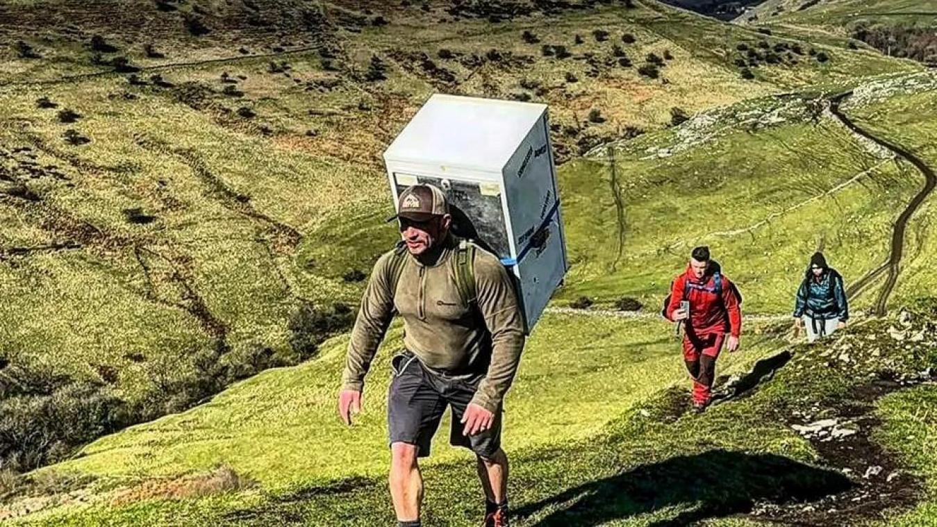 WTF. Man wil drie bergtoppen beklimmen met koelkast op zijn rug
