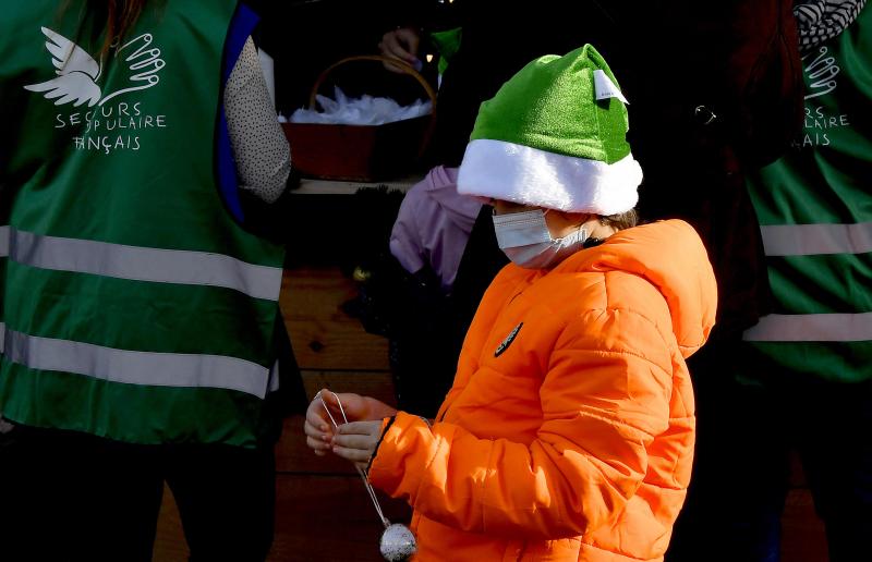 A boy stands by volunteers as recipients attend the Christmas event of French charity Secours Populaire Français in Toulouse on December 22, 2020. - Most of Toulouse families invited for Secours populaire Christmas event are coming for the first time, hit hard by the Covid-19 crisis. (Photo by GEORGES GOBET / AFP)