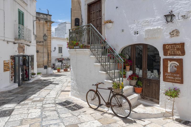 Old bicycle in front of a white wall with stairs and brown wooden doors in the city Ostuni, Apulia, southern Italy.